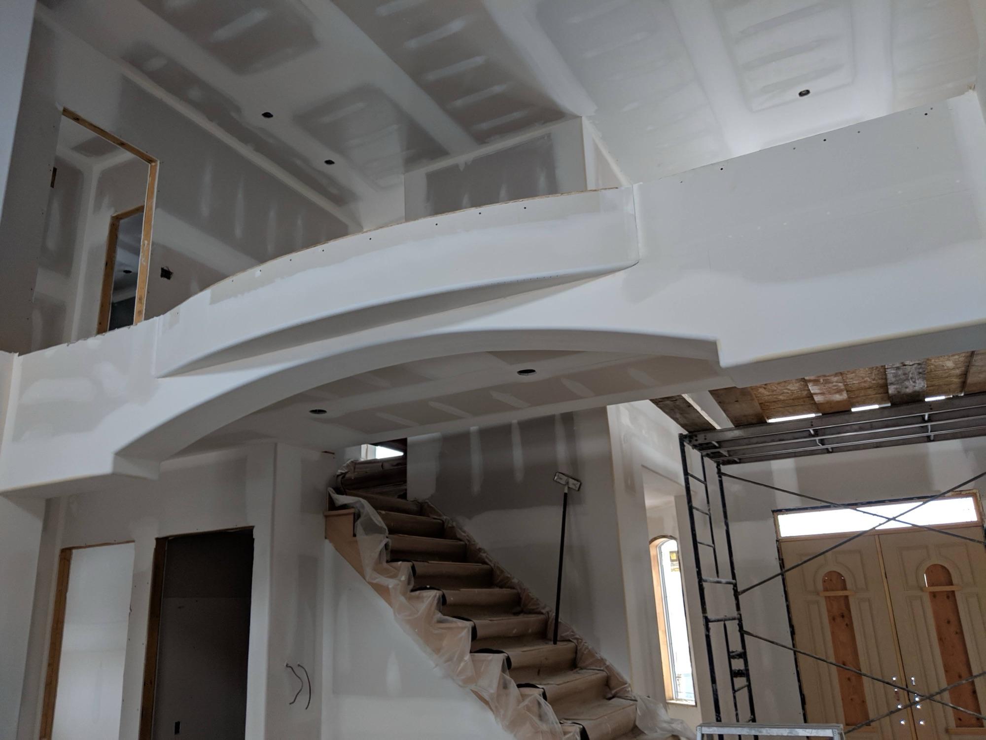 A curved drywall arch over a staircase, taped and sanded ahead of primer in a two-storey foyer